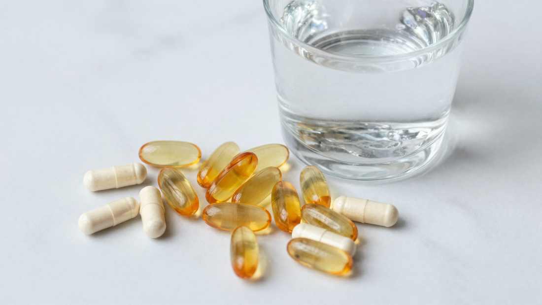 Vitamin capsules beside a glass of water on marble