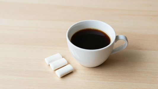 A cup of black coffee beside chewing gum on a table